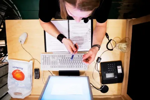 Person vid skrivbord med dator, telefon och papper. Kanske arbetar med lagen om distansavtal.