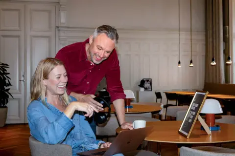 En it-specialist hjälper en kollega med en laptop. De skrattar tillsammans i en ljus lokal.