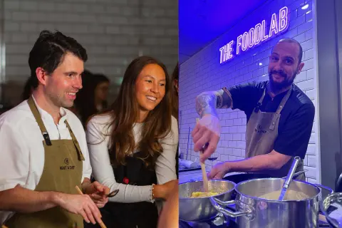 Två glada personer deltar i roliga kurser i matlagning. En man och en kvinna ler medan de lagar mat, och en kock med tatueringar rör i kastruller under neonskylten "THE FOODLAB".