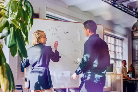 Kvinnlig och manlig kollega diskuterar på whiteboard, en del av en cloud engineer utbildning.