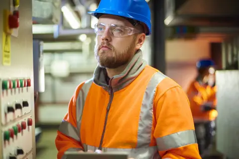 Man i blå hjälm och varselkläder vid kontrollpanel. En del av en produktionstekniker utbildning.