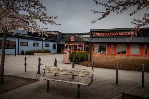 Angeredsgymnasiet i vårskrud med blommande träd. En bänk står tom på skolgården.