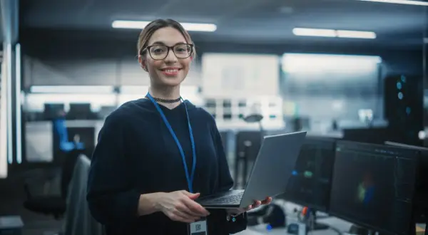 En kvinna med glasögon håller en laptop i ett modernt kontor, redo för sin cyber security utbildning distans.