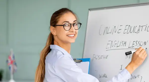 Glad lärare skriver "English Lesson" på en whiteboard. Perfekt för din engelska kurs distans.