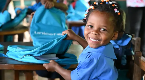Glad flicka i blå skoluniform öppnar en UNICEF-väska i en skola.