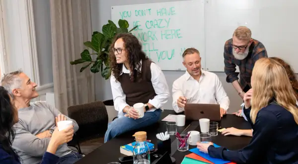 Teammedlemmar diskuterar vid ett bord. En person som ser ut som en facility manager ler.