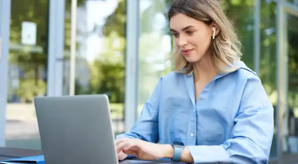 Kvinna med hörlurar arbetar på laptop utomhus, drömmer om bra betalda jobb utan utbildning.
