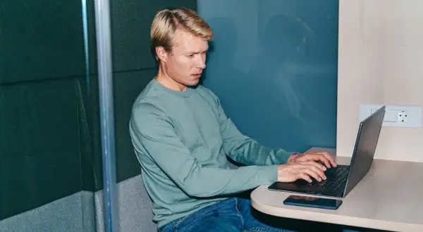 Man i ljudisolerad bås jobbar intensivt på laptop, kanske funderar på konsekvenserna av illojalitet mot arbetsgivare och skadestånd.