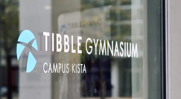 Tibble Gymnasium, Campus Kista. En blå logotyp och vit text på en glasdörr.