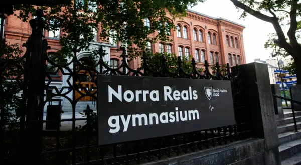 Skylt med texten "Norra Reals gymnasium" framför en vacker tegelbyggnad.
