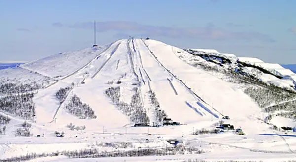 Snöklädda pister på ett berg med en mast på toppen, en vy som påminner om rymdgymnasiet Kiruna.