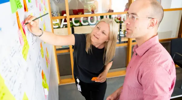 En ux designer pekar på en whiteboard med post-it-lappar.