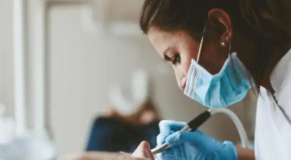 En tandhygienist i mask och handskar arbetar med en patient. En del av tandhygienist utbildning.