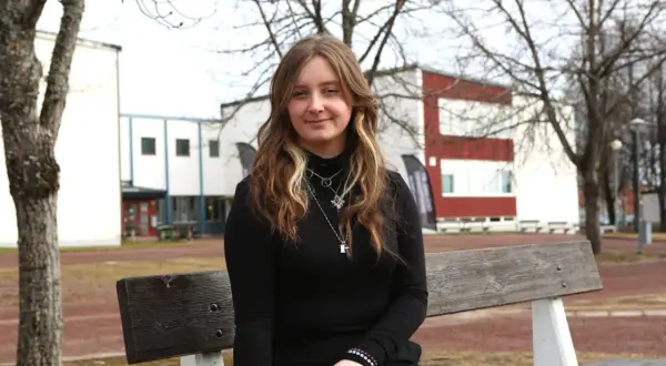Ung kvinna sitter på en bänk utanför en skolbyggnad. Hon hoppas på ett stipendium för gymnasiet.