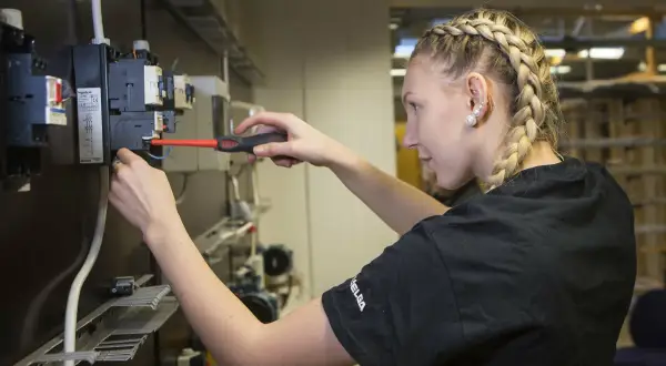 En ung kvinna med flätat hår arbetar med elinstallationer, en framtida elektriker från gymnasiet.