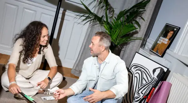 Två personer diskuterar en digital strateg. En kvinna med lockigt hår och en man med grått hår sitter på golvet.
