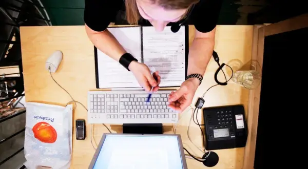 Person vid skrivbord med dator, telefon och papper. Kanske arbetar med lagen om distansavtal.
