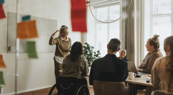 En social media manager presenterar idéer för sitt team. En kvinna i rullstol deltar i mötet.