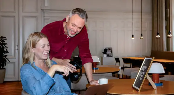 En it-specialist hjälper en kollega med en laptop. De skrattar tillsammans i en ljus lokal.