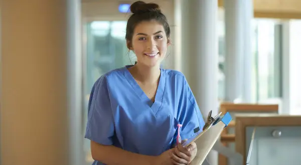 Glad ung kvinna i blå scrubs med en clipboard, redo för sin laborant utbildning.