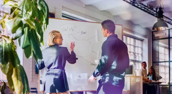 Kvinnlig och manlig kollega diskuterar på whiteboard, en del av en cloud engineer utbildning.