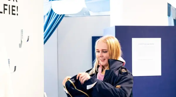 Glad tjej med ljusblont hår, klädd i mörkblå jacka, tittar ner på en väska. Hon är på ett event för ett vf gymnasieprogram.