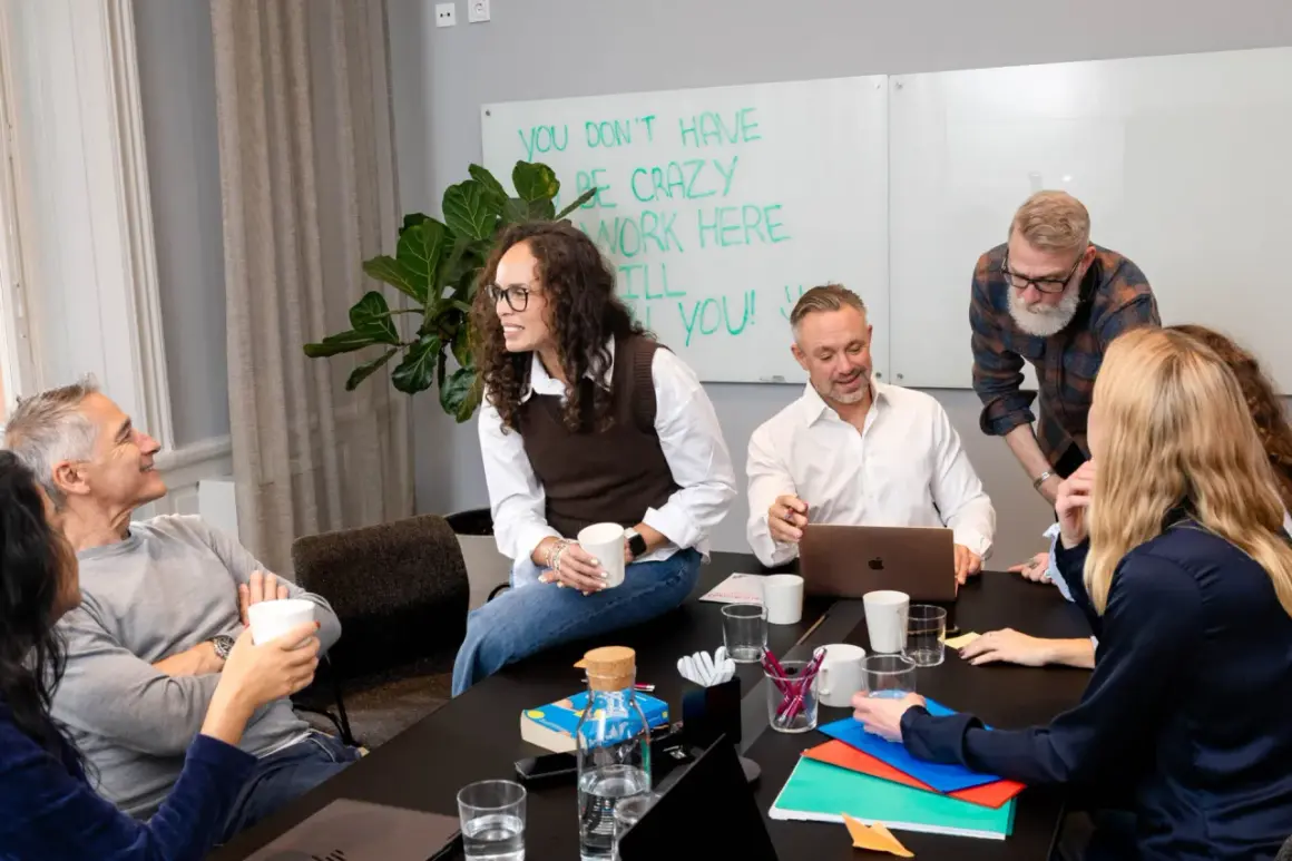 Teammedlemmar diskuterar vid ett bord. En person som ser ut som en facility manager ler.