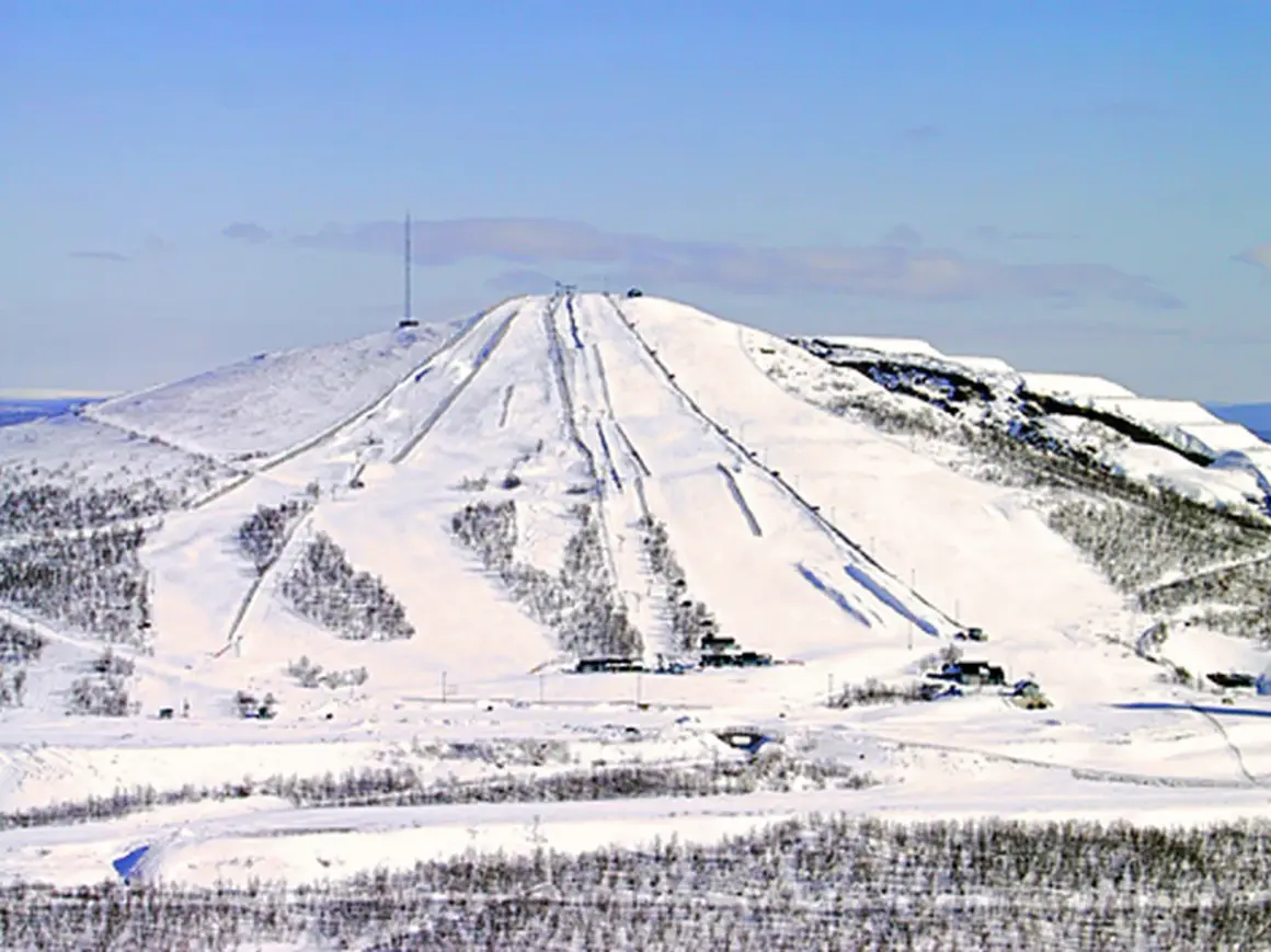 Snöklädda pister på ett berg med en mast på toppen, en vy som påminner om rymdgymnasiet Kiruna.
