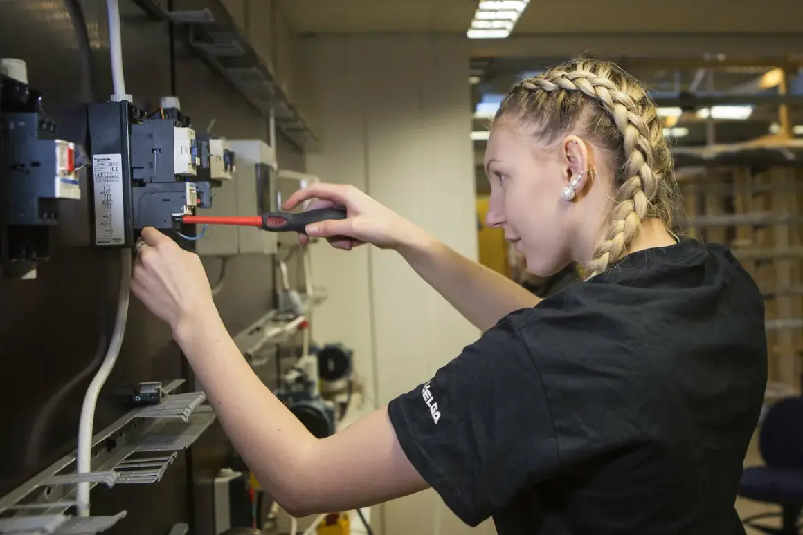 En ung kvinna med flätat hår arbetar med elinstallationer, en framtida elektriker från gymnasiet.