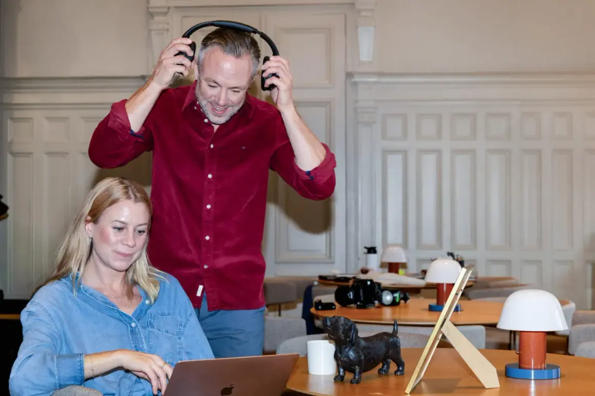 Man med hörlurar och kvinna vid laptop, en hundstatyett på bordet. De arbetar med sitt it konsult-projekt.