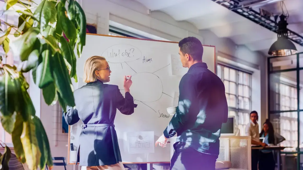 Kvinnlig och manlig kollega diskuterar på whiteboard, en del av en cloud engineer utbildning.