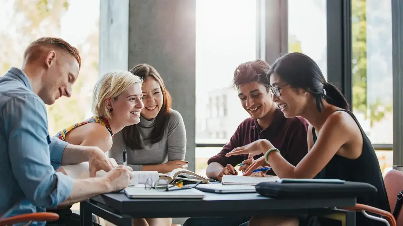 Glada studenter vid Grit Academy diskuterar ivrigt vid ett bord med b&ouml;cker och anteckningar.