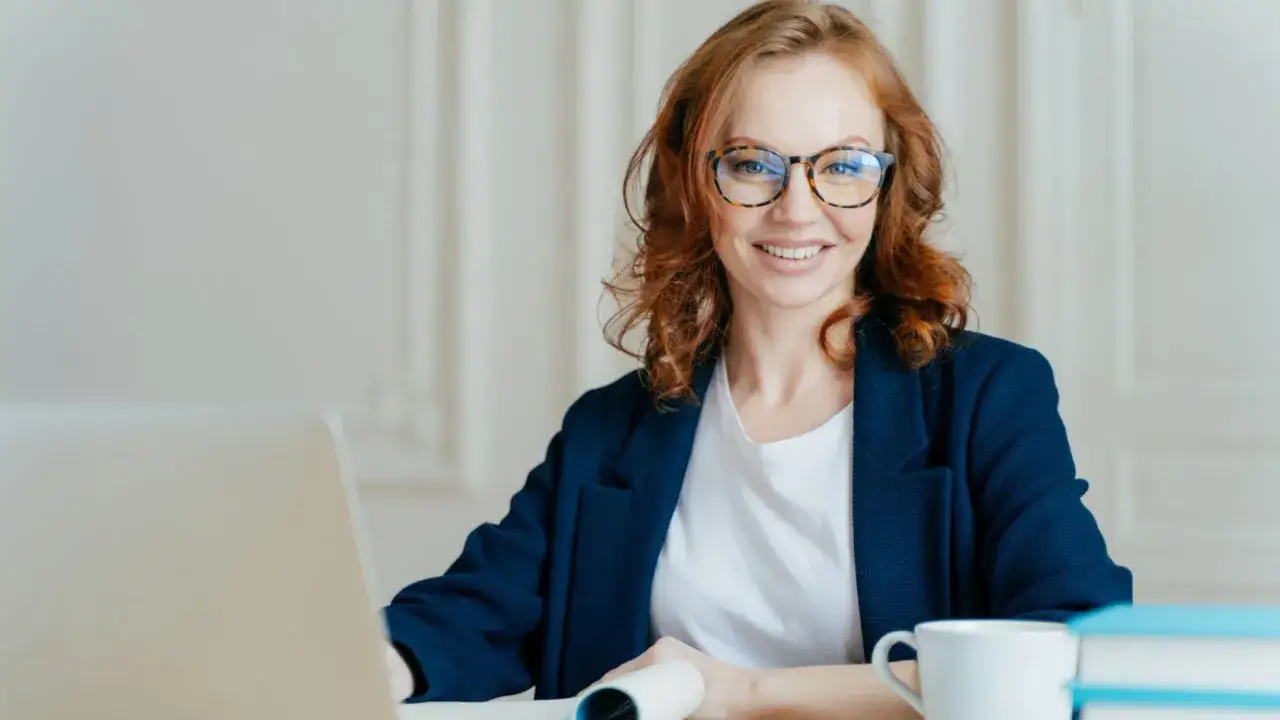 Glad kvinna med glas&ouml;gon vid skrivbordet, redo f&ouml;r sin hr business partner utbildning.