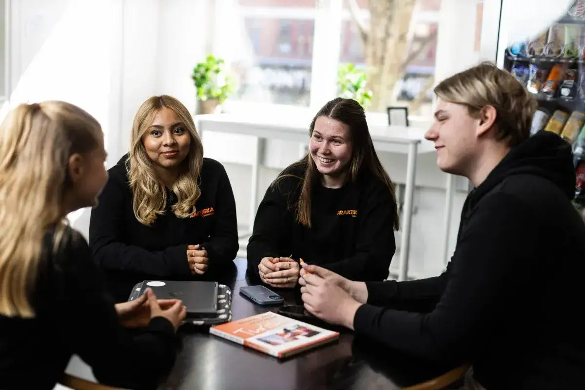 Fyra elever fr&aring;n Praktiska gymnasiet Kristianstad sitter samlade runt ett bord och samtalar.