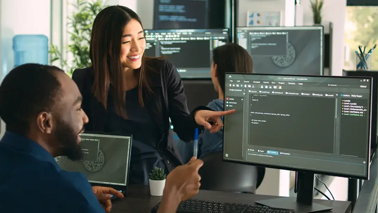 Kvinnlig programmerare pekar p&aring; kod p&aring; en sk&auml;rm, diskuterar med manlig kollega. De &auml;r p&aring; Chas Academy och l&auml;r sig nya saker.