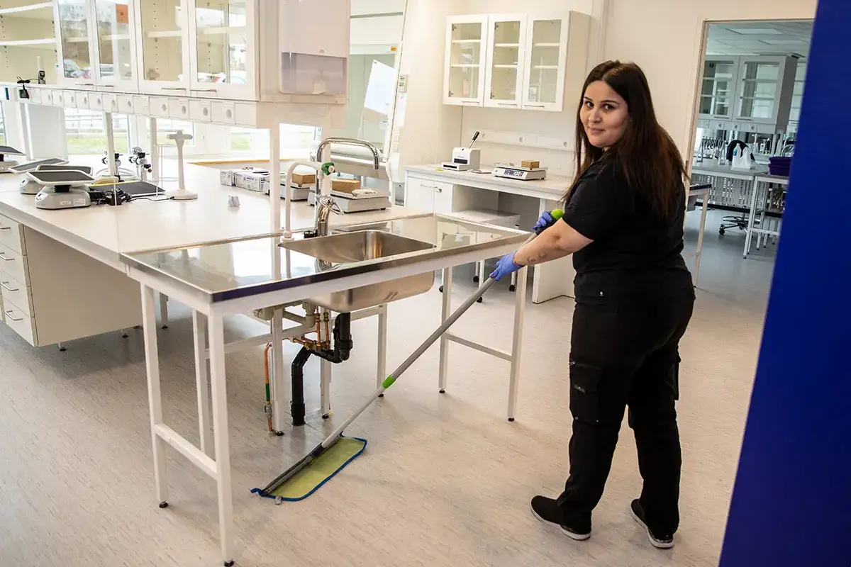 En kvinna, som ser ut att vara en facility manager, st&auml;dar ett laboratorium med en mopp.