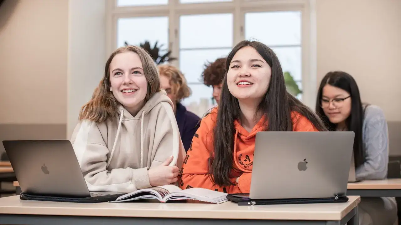 Elever p&aring; nti vetenskapsgymnasiet Stockholm ler under en lektion, med laptops och b&ouml;cker framf&ouml;r sig.