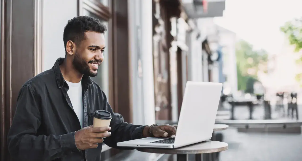Man med kaffe och laptop utomhus, kanske pluggar kbt utbildning distans.
