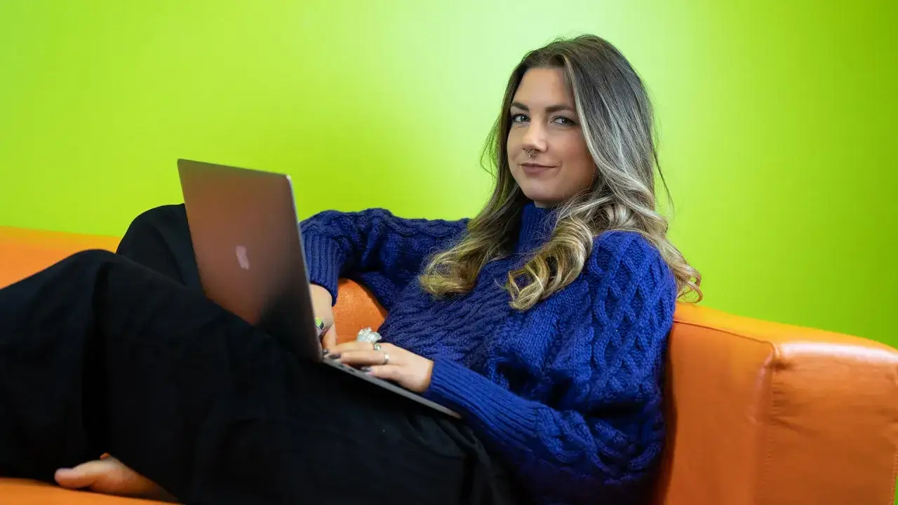 Kvinna med laptop p&aring; orange soffa, med gr&ouml;n v&auml;gg i bakgrunden. Hon arbetar troligen med Medlearn AB.