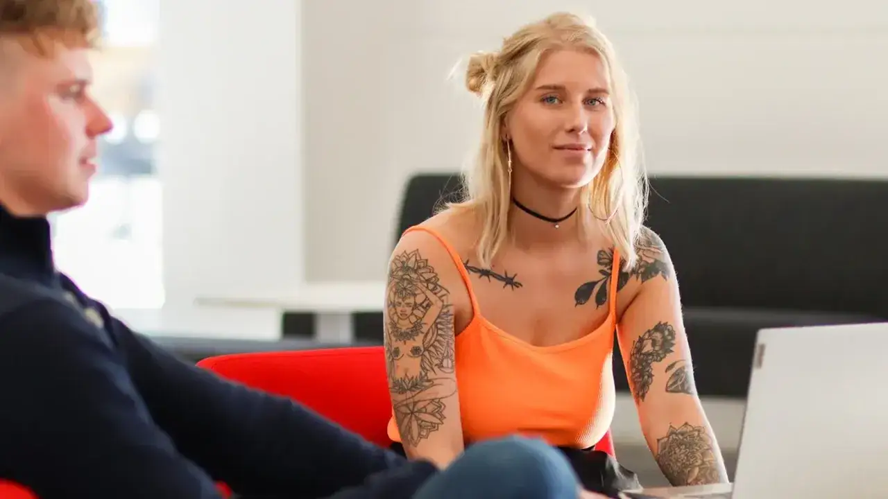 Tv&aring; personer diskuterar webbutveckling utbildning vid en laptop. Kvinnan har tatueringar p&aring; armarna.