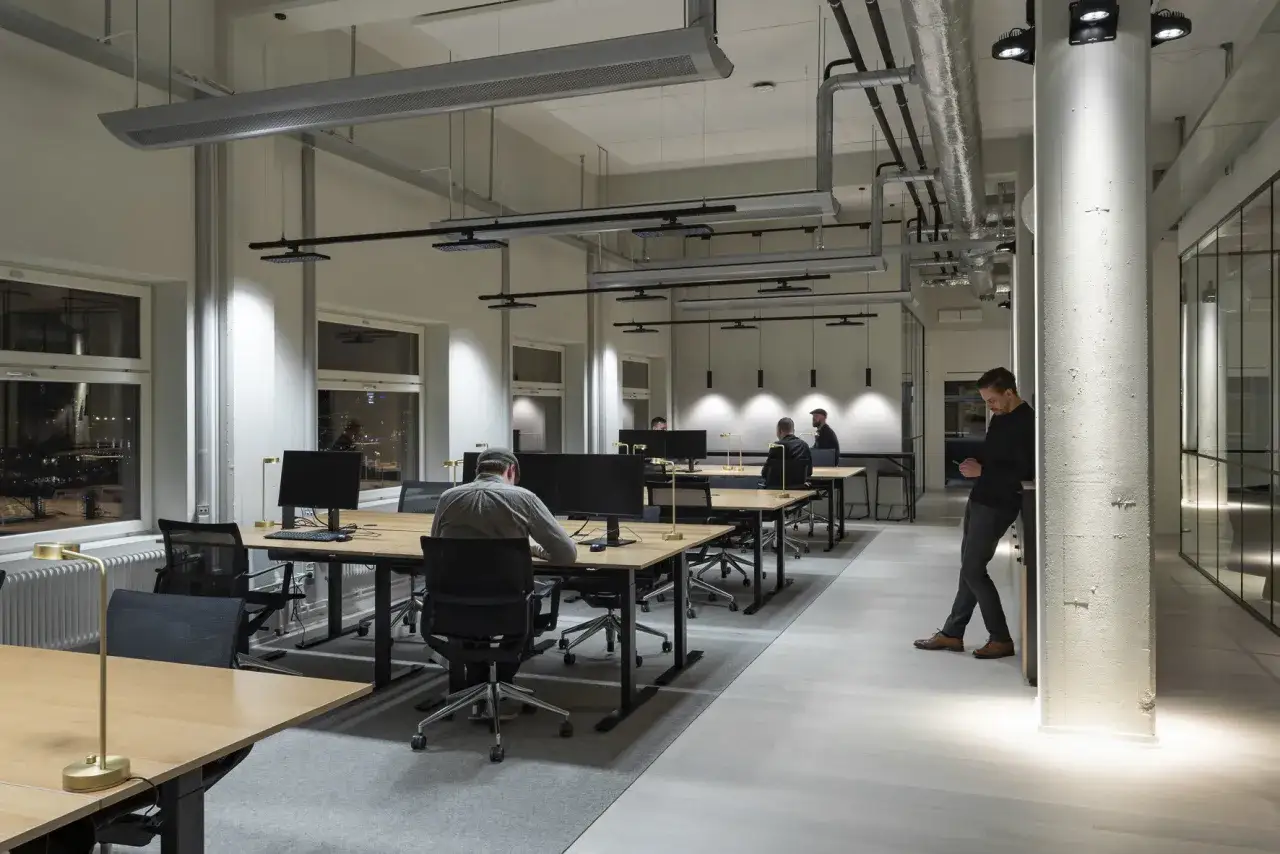 En it-specialist tar en paus vid en pelare i ett modernt kontorslandskap med m&aring;nga arbetsplatser.