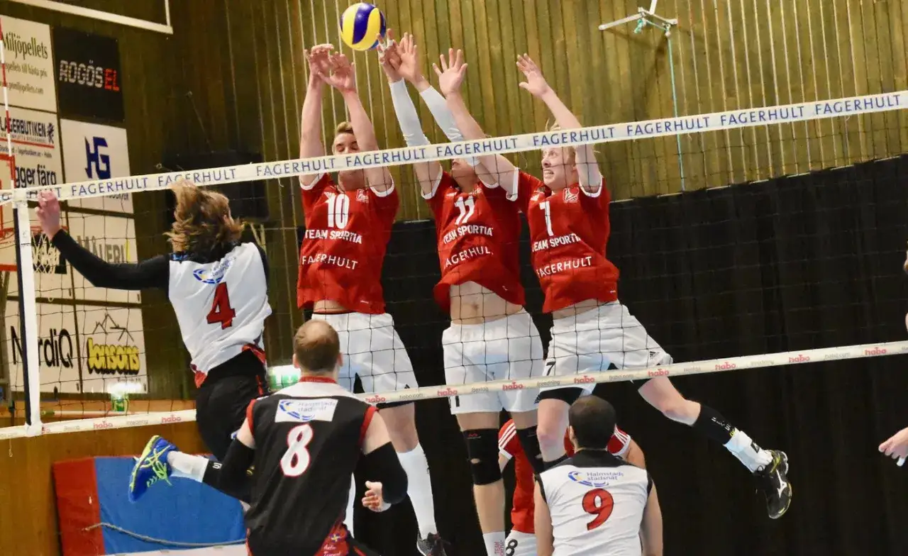 Volleybollspelare hoppar f&ouml;r att blockera vid sanda gymnasiet. Spelare i r&ouml;da tr&ouml;jor med nummer 10, 11 och 1.