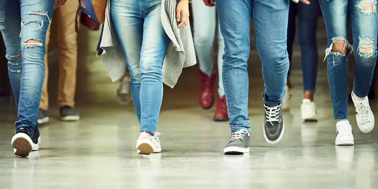 Ungdomar i jeans och sneakers g&aring;r i en korridor. Kanske p&aring; v&auml;g till en lektion med fri kvot gymnasiet.