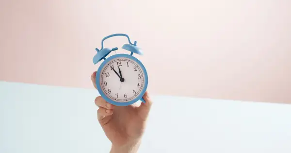 En hand håller en blå väckarklocka. Snart är det dags för antagningsbesked gymnasiet!