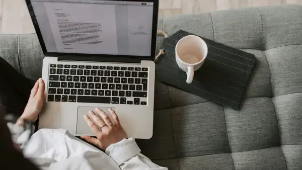 Person som arbetar med e-learning på en laptop i soffan, med en kaffekopp bredvid.