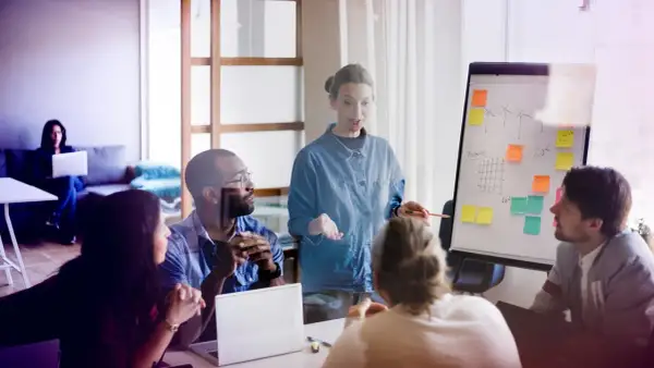 Mötesdeltagare diskuterar en presentation om hållbarhet, liknande en byggnadsantikvarie utbildning. En kvinna leder diskussionen vid en whiteboard.