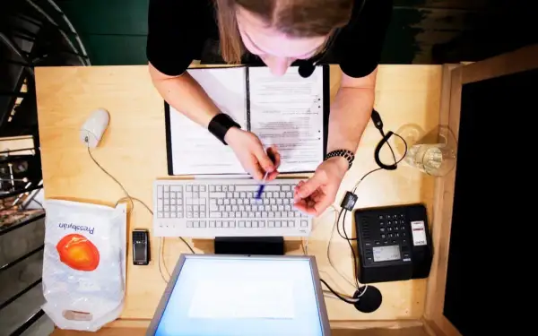 Person vid skrivbord med dator, telefon och papper. Kanske arbetar med lagen om distansavtal.