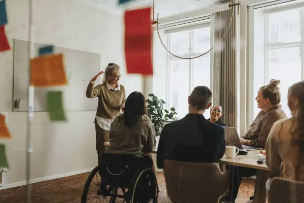 En social media manager presenterar idéer för sitt team. En kvinna i rullstol deltar i mötet.
