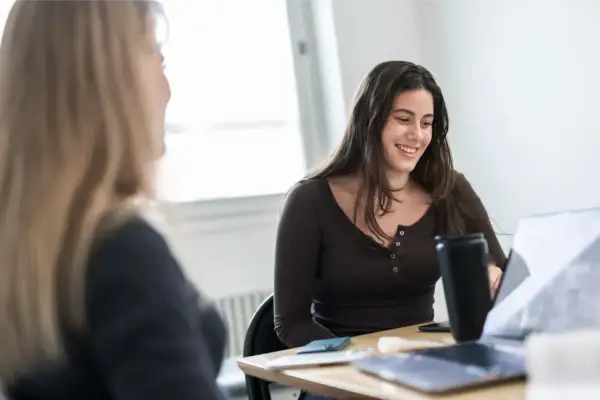 Två studenter diskuterar sina studier inom kiropraktor utbildning vid ett bord med laptops.