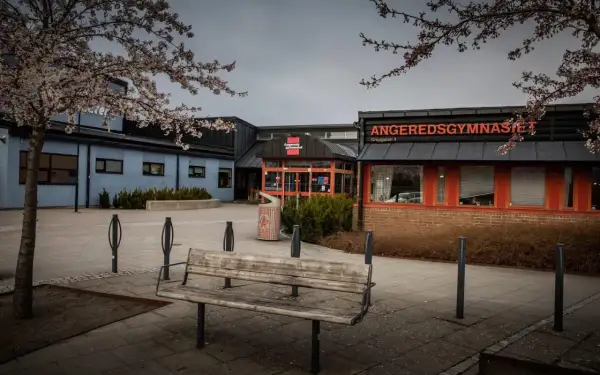 Angeredsgymnasiet i vårskrud med blommande träd. En bänk står tom på skolgården.
